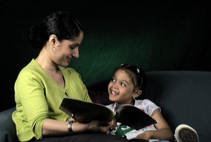 A mother reads to her daughter on a couch.