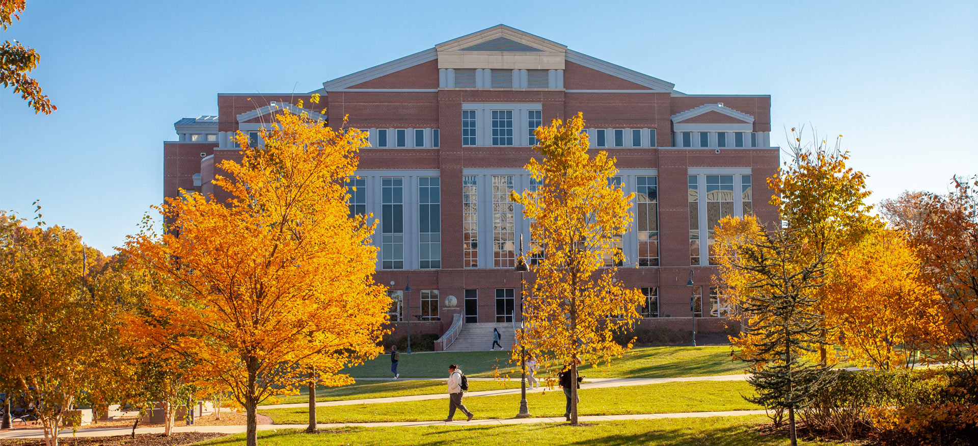 student walking in front of library with fall foliage