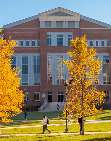 student walking in front of library with fall foliage
