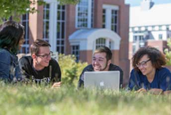 students laying in grass on computer