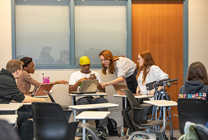 professor leaning over desk to help students with classwork