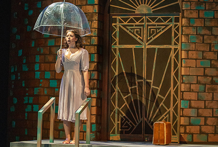 student actor on stage holding an umbrella in front of a backdrop of a building