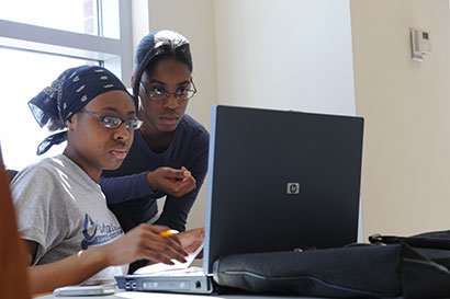 Decorative image of two students using a laptop