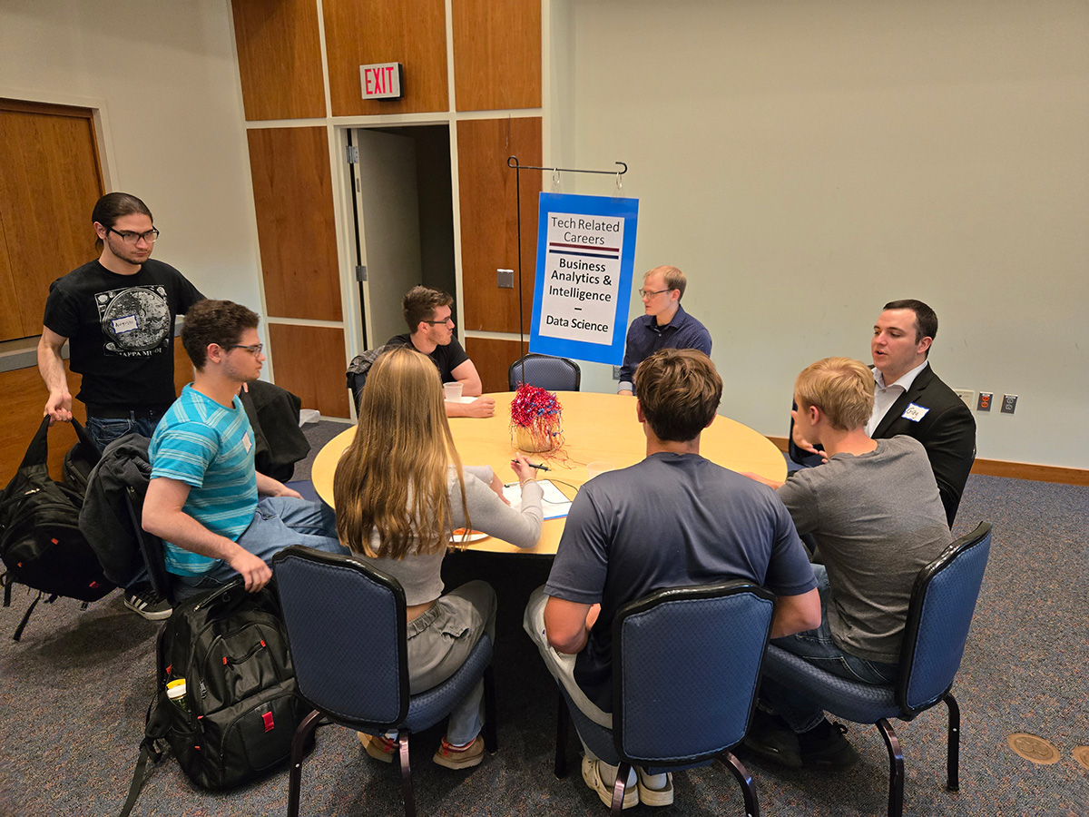 students and professors sitting at a table with a sign that reads 'Tech Related Careers Business Analytics & Intelligence - Data Science' on it