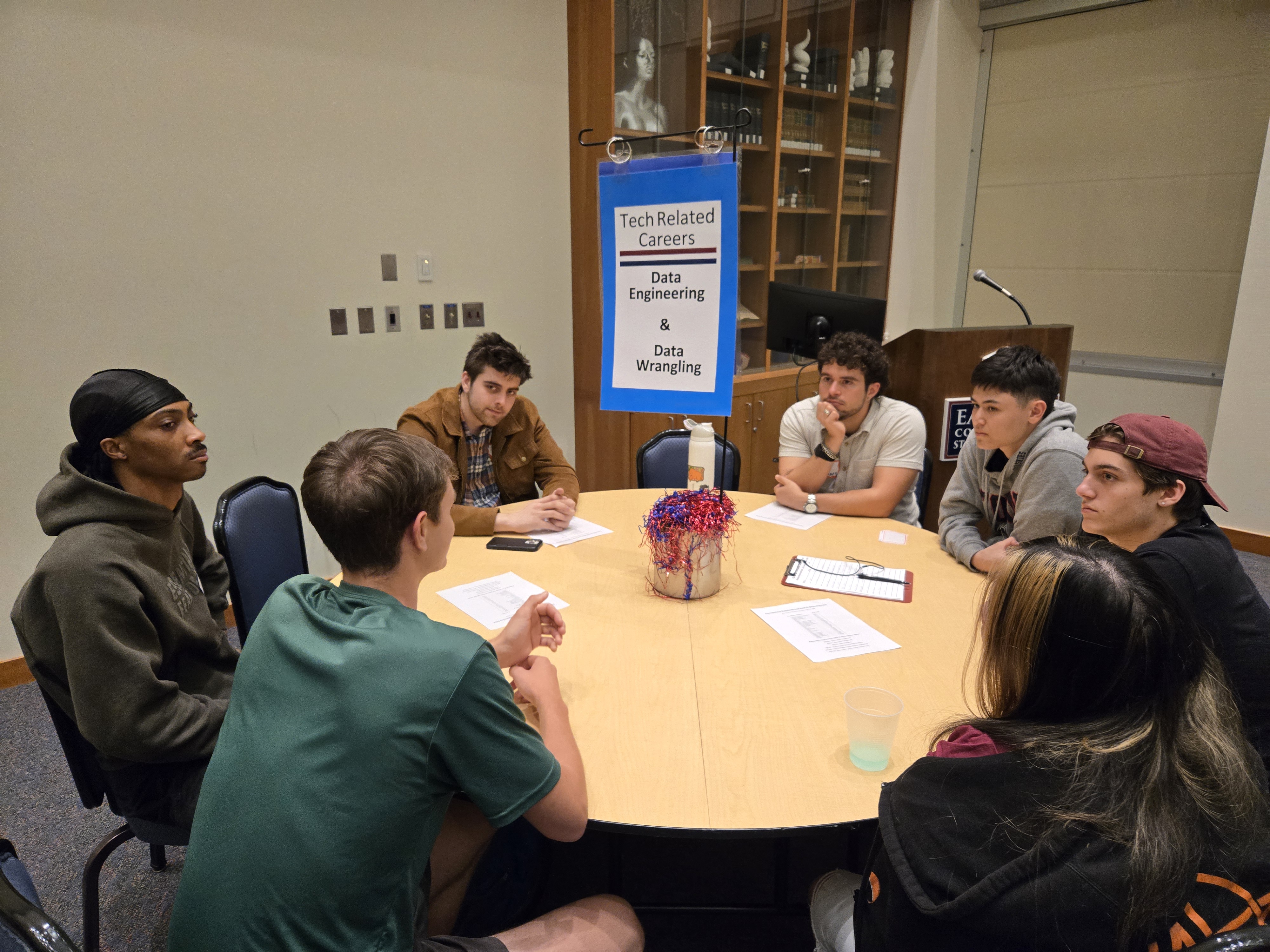 student sitting around a table with a sign that reads 'Tech Related Careers Data Engineering & Data Wrangling' behind them