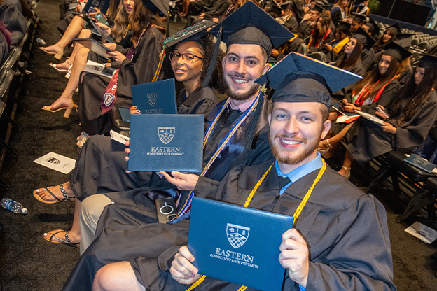 graduates showing the camera their diploma covers