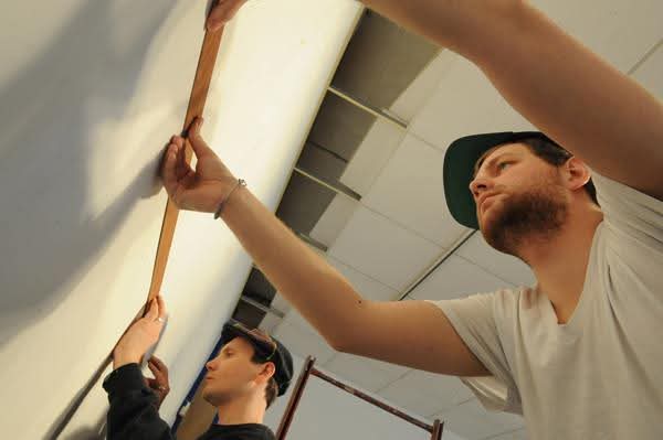 two men holding up paneling against the wall of Akus Gallery