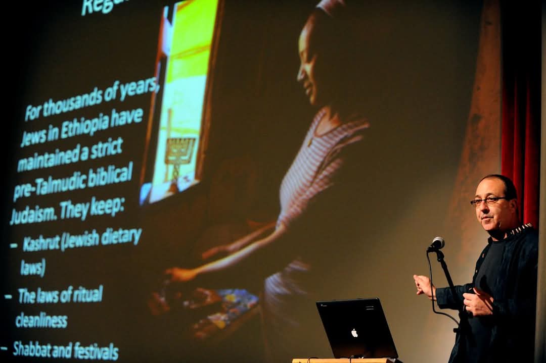 a presenter on stage with a projection in the background during the Jewish exhibition