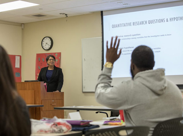 Professor standing in front of class while student raises hand