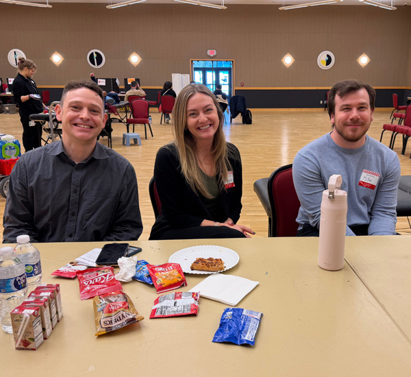 Staff members posing for photo at blood donation event with food on the table in front of them