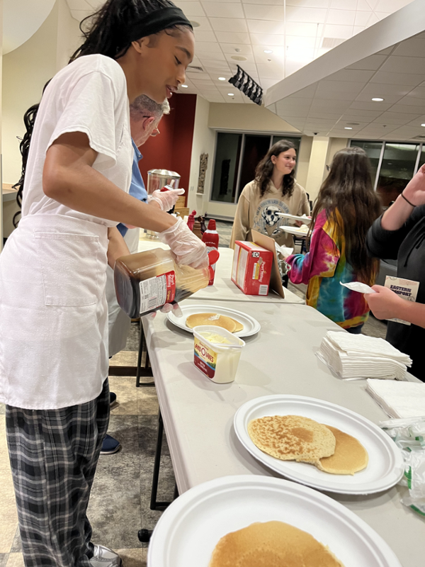 Student worker serving pancakes to a line of students.