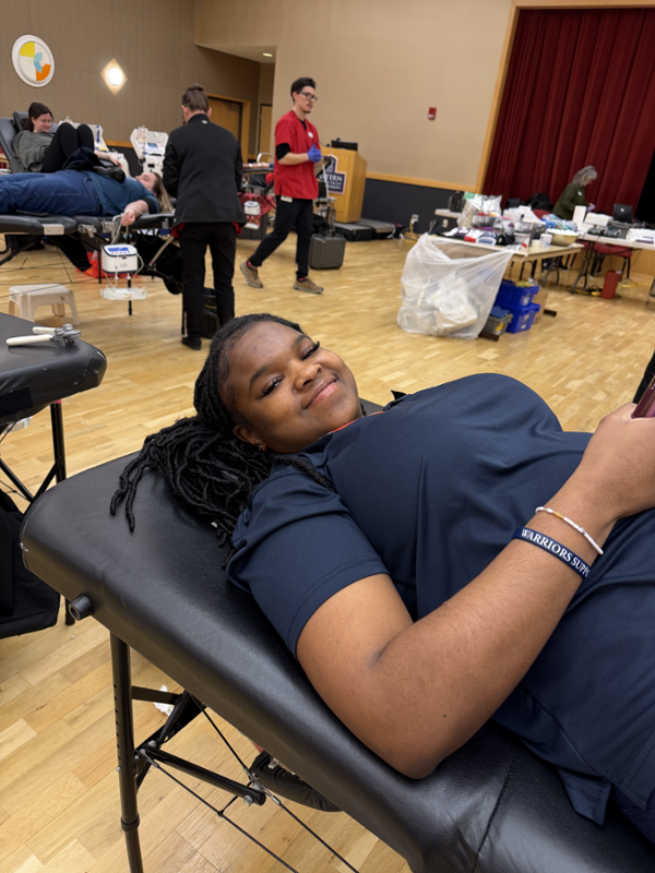 Student is donating blood at a blood drive with a big smile.