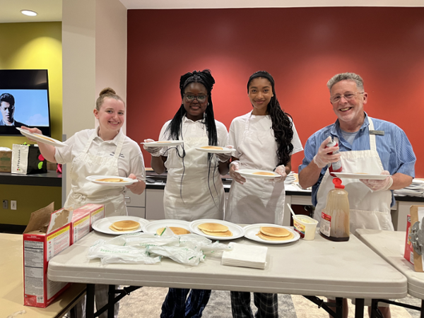 students standing behind a table with plates of pancakes on it