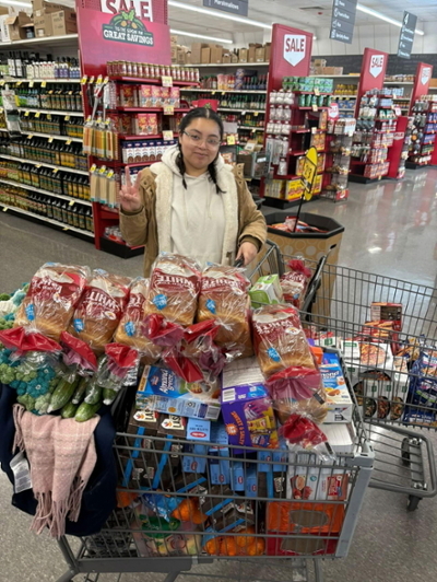 Zaine, the volunteer coordinator previously, pushing a shopping card loaded with food items
