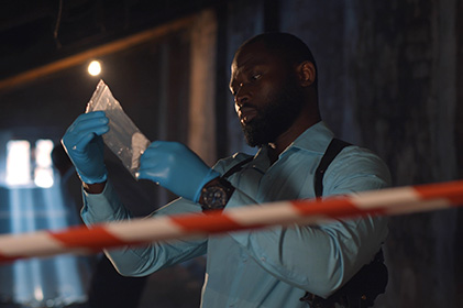 police detective looking at bagged evidence with red/white striped barrier tape in the foreground