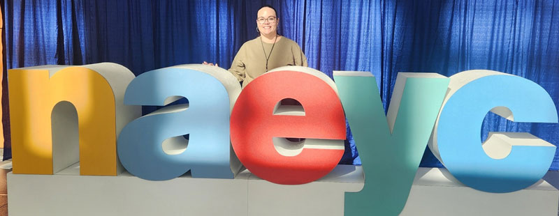 Karla Alamo poses with the NAEYC logo at the Washington Convention Center.