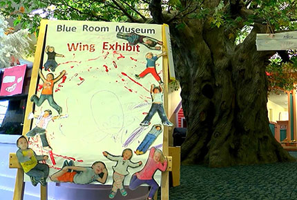 A sign with the words "Blue Room Museum Wing Exhibit" and cut-out images of children in various positions around the perimeter of the sign