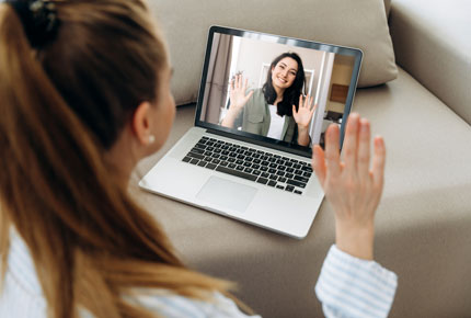  A woman waving to another woman through a video chat on a laptop. 