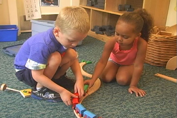 Two children play with trains and tracks. 
