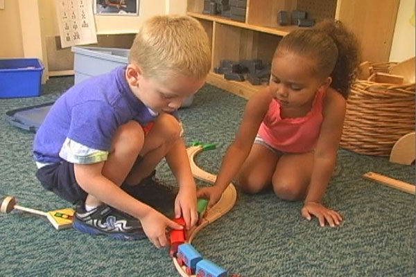 Two children play with trains and tracks.