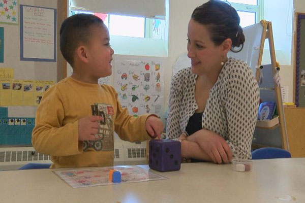 A teacher and child smile at each other while playing a board game. 