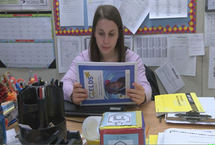 A teacher sits at her desk and reads the CT Early Learning Standards and Development Standards guide