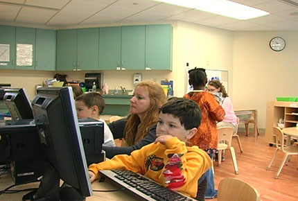 A teacher sits with a preschooler using a computer