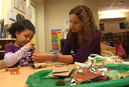 A teacher assists a preschooler in cutting a paper towel tube
