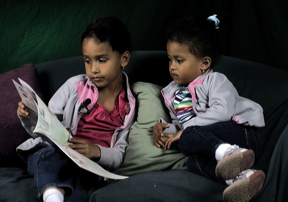 Two sisters reading on the couch. 