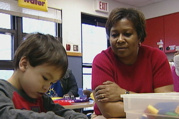 A teacher sits with a child who is building with legos. 