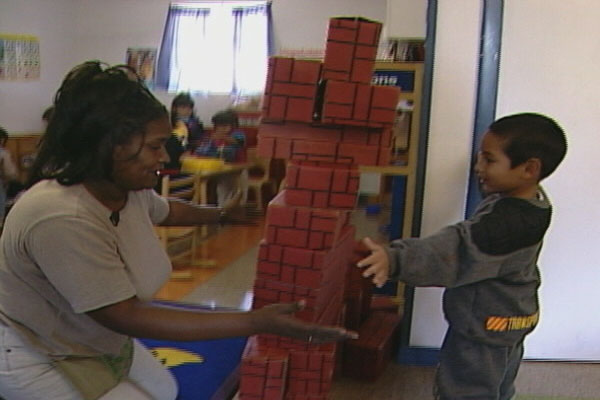 A teacher building with a child in the block area. 