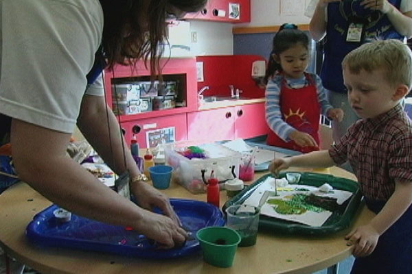 A teacher helps a child get set up at the art table. 