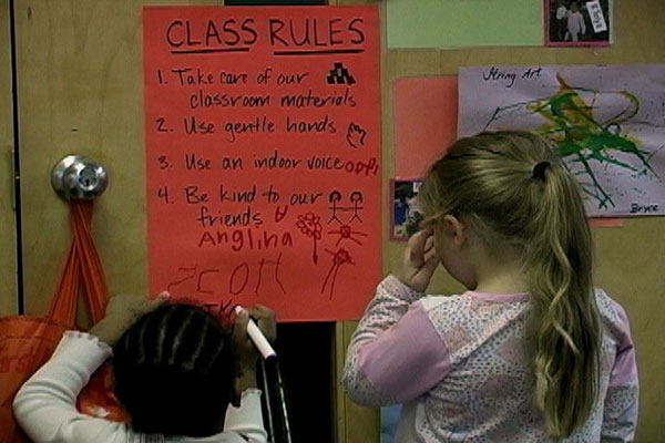 Two children read a poster of Classroom Rules.