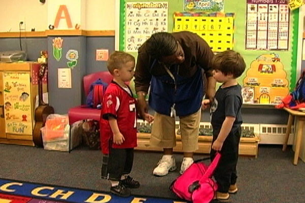 A teacher stand between two children and helps them through a conflict.