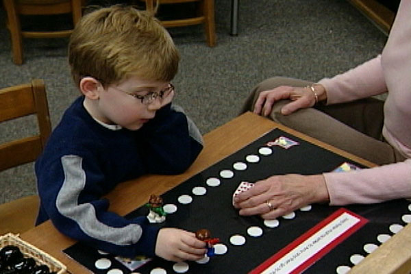 A child sits with a teacher at a table working on an activity. 