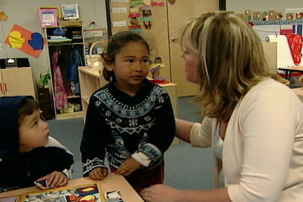 A woman talks with a child and has her hand on the child's back.