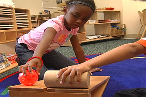 A child rolling a ball down a wooden ramp. 