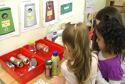 Preschoolers stand in front of bins to sort recycling