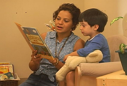 A child sits in his teachers lap as she read him a book.