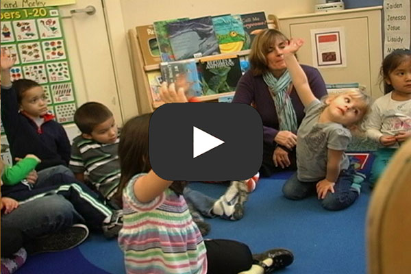 Children and teachers sit on the floor listening to a story. 