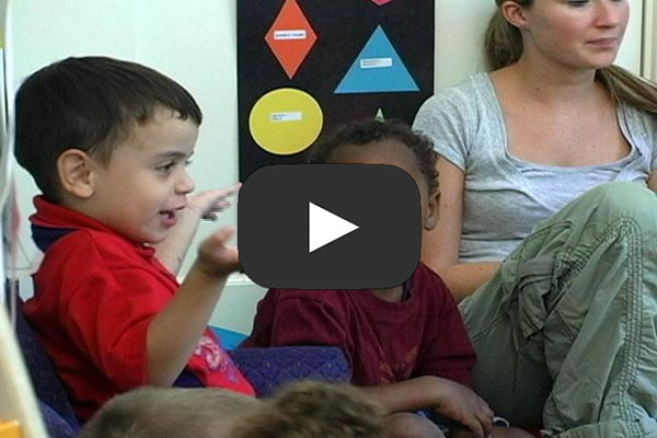 Children and teachers sit on the floor. A child is speaking. 