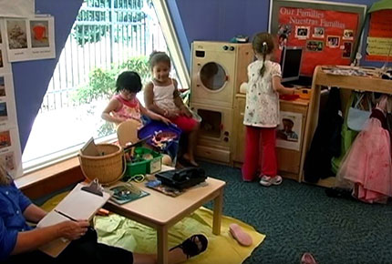 A teacher watches as children use dramatic play items to tell a story.