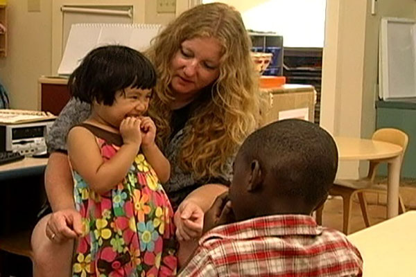 A teacher sits and talks with two children.