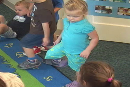 A group of preschoolers dance to a song during a whole group activity.