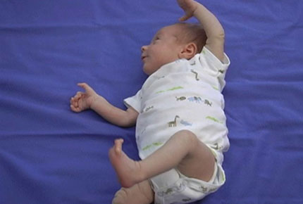 A tiny infant lies on his back on a blanket with arms and legs raised in the air