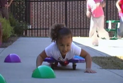 A child lays on her belly on a scooter and moves through an obstacle course.