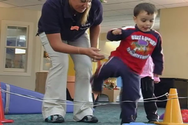 A teacher helps a child step over an obstacle.