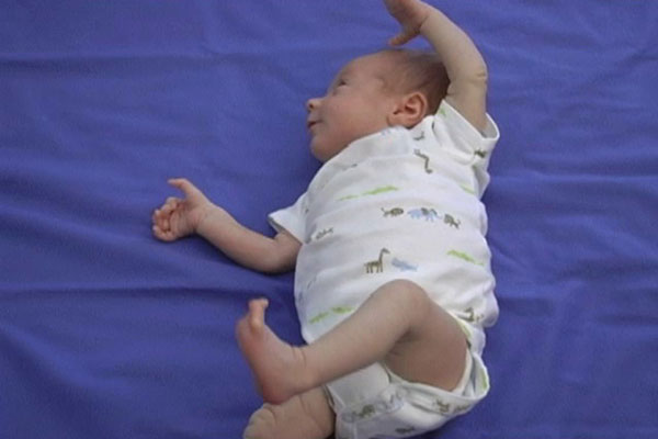An infant lays on a blanket on his back and moves his arms and legs.
