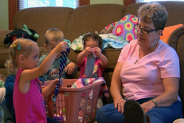 Children sit on the floor with their teacher as they sort socks from a laundry basket.