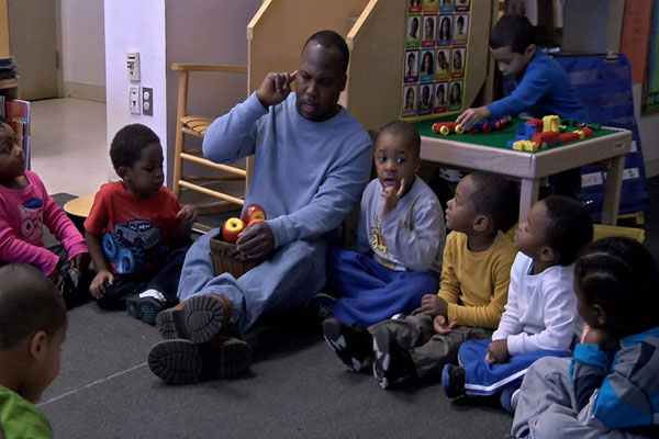 A teacher and several students sit on the floor in a circle